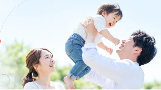 父親が子どもを高く抱き上げ、母親が見守っている様子