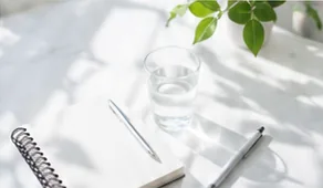 ノートとペン、水の入ったグラスと観葉植物を並べた机