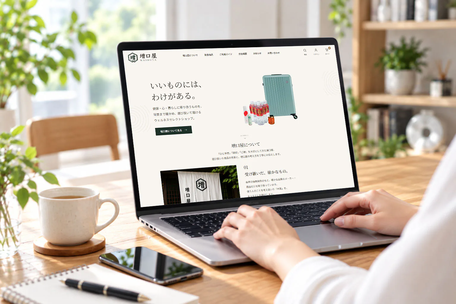 ノートパソコンで自社ECサイト「増口屋」のトップページを開いている手元と、コーヒーカップ